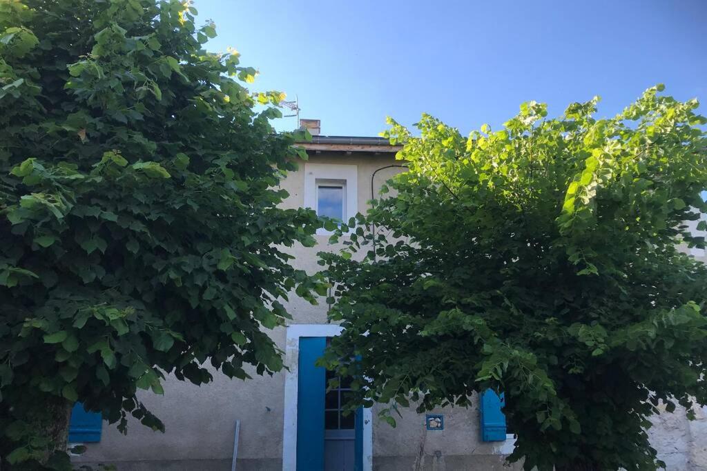 a building with a blue door between two trees at MAISON RESTAUREE 6 PERSONNES AU COEUR DU PERIGORD in Sourzac