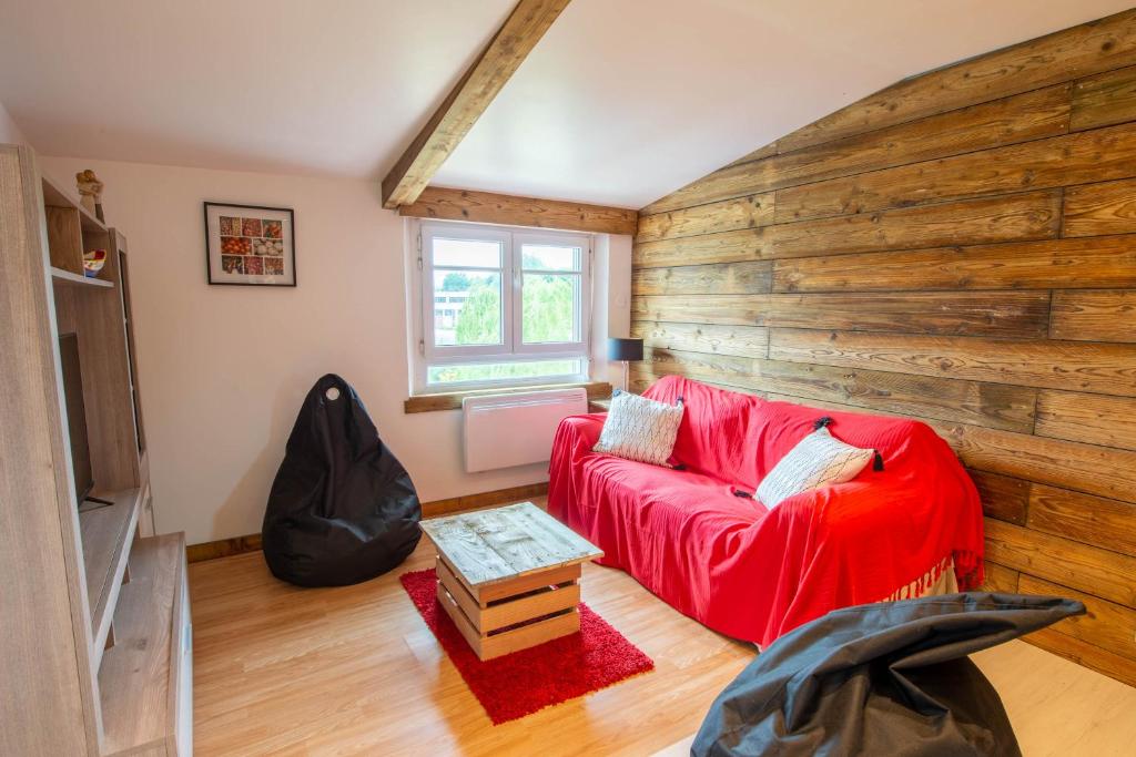 Gîte Plume et Potiron في جيزور: غرفة معيشة مع أريكة حمراء وجدار خشبي