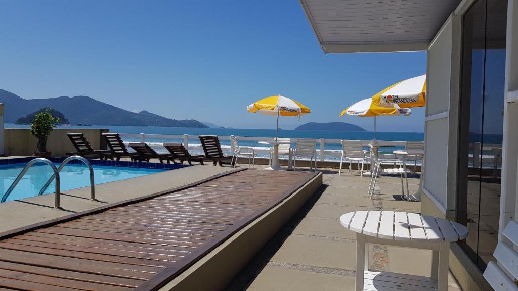 einen Pool mit Stühlen und Sonnenschirmen am Strand in der Unterkunft Hotel Maranduba in Ubatuba