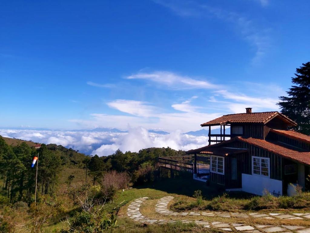a building on top of a mountain with clouds in the background at Chalé no mar de nuvens - Serra da bocaina in São José do Barreiro
