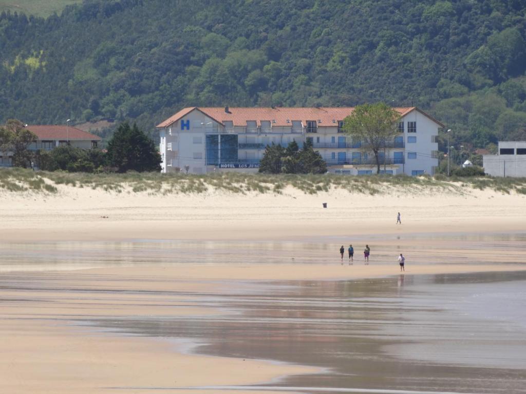 due persone che camminano su una spiaggia con un edificio sullo sfondo di Hotel Los Juncos a Noja