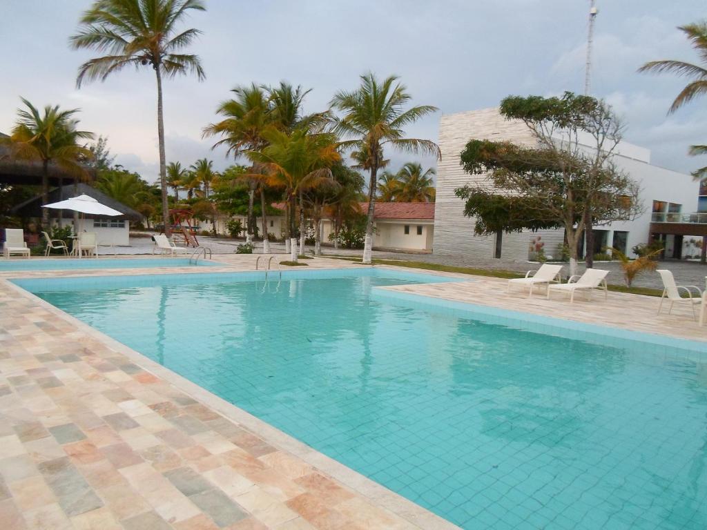 a large swimming pool with palm trees and a building at Hotel Abrolhos in Nova Viçosa