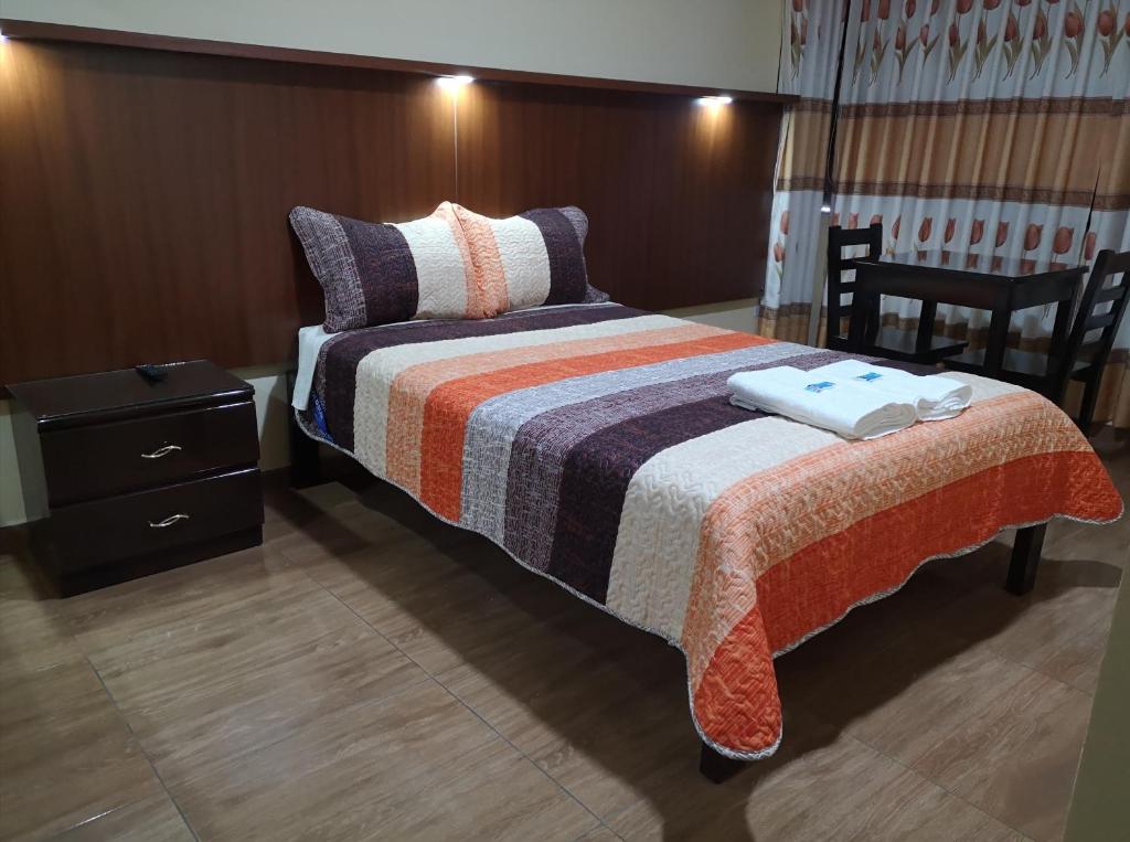 1 dormitorio con 1 cama con manta a rayas y mesita de noche en Lembranças Hotel, en Huánuco