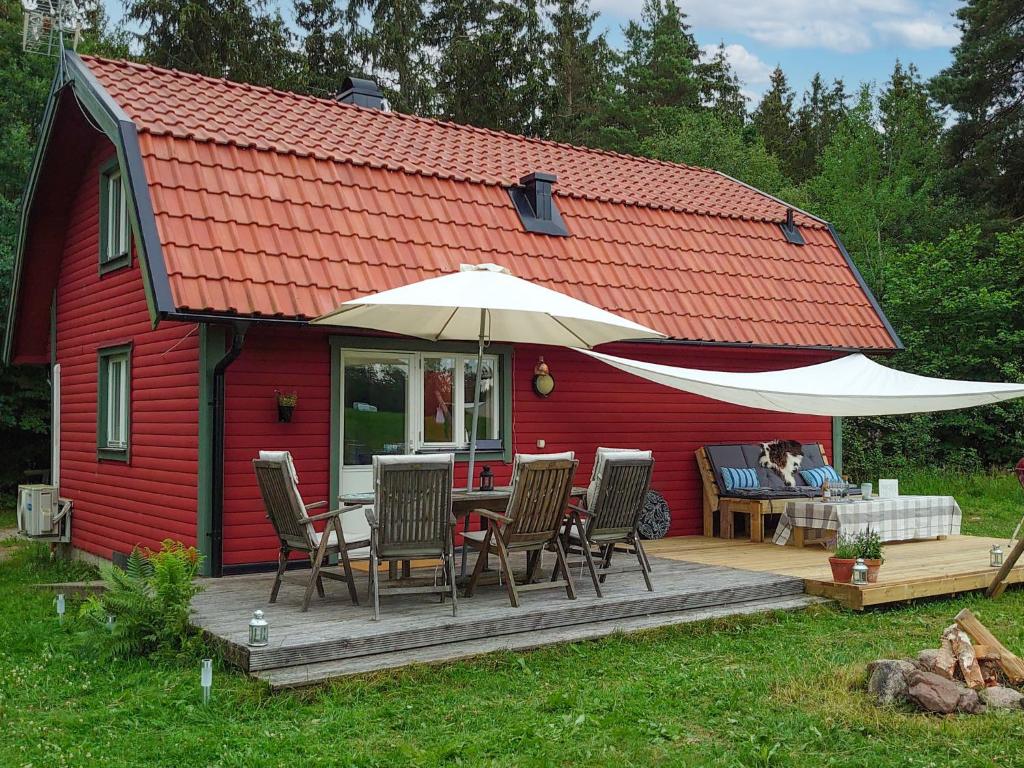 een rood huis met een tafel en stoelen en een paraplu bij Chalet Grönede - OST006 by Interhome in Kisa