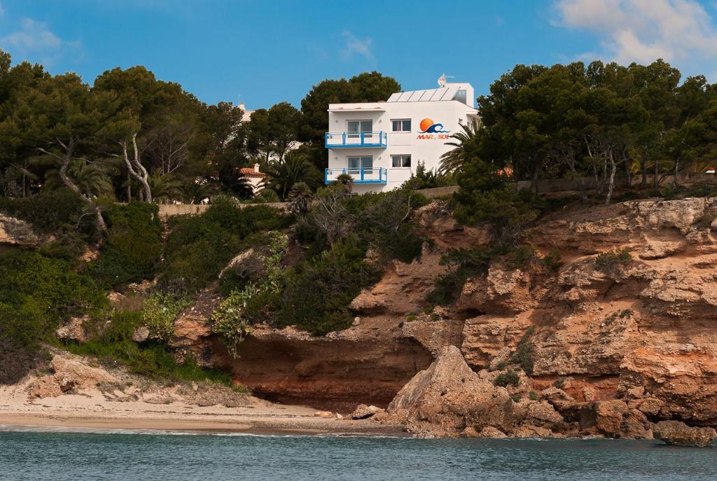 a white house on a cliff next to a beach at Apartamentos Mar y Sol in Miami Platja