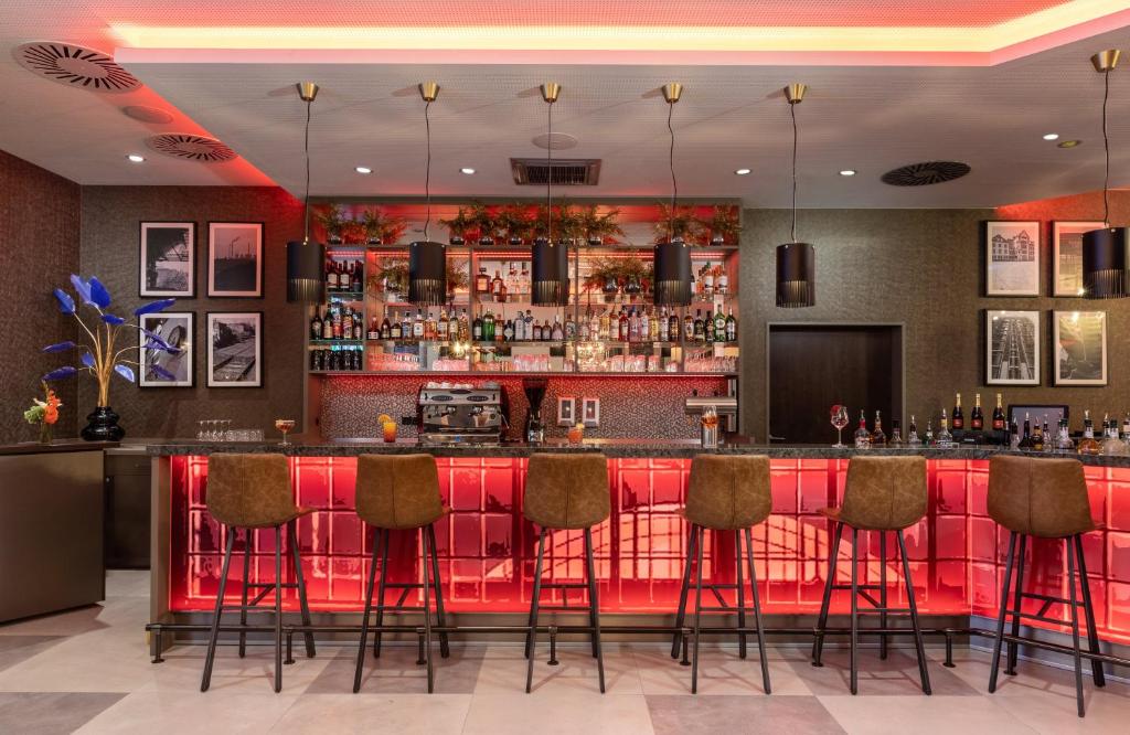 a bar at a restaurant with red bar stools at Leonardo Hotel Dortmund in Dortmund