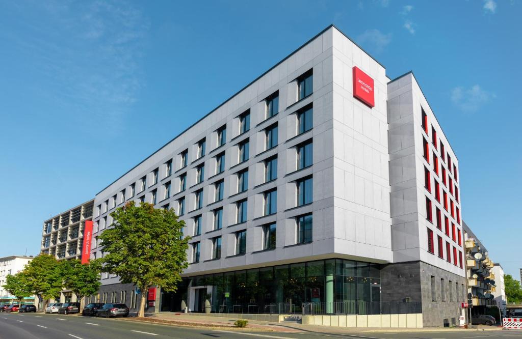 a tall white building with a red sign on it at Leonardo Hotel Dortmund in Dortmund