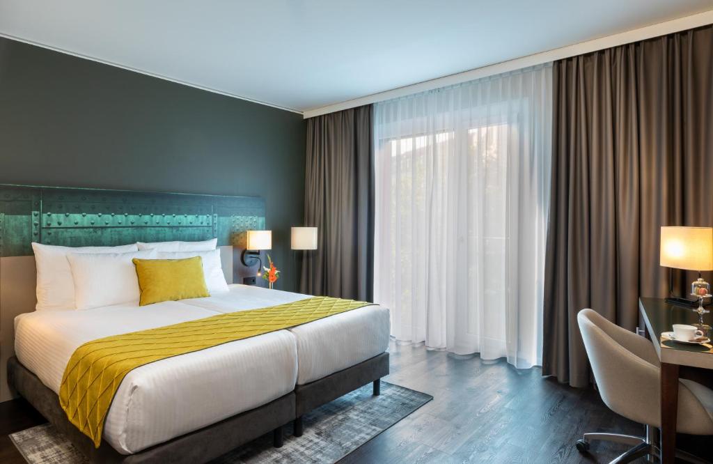 a bedroom with a large bed and a desk with a desk at Leonardo Hotel Dortmund in Dortmund