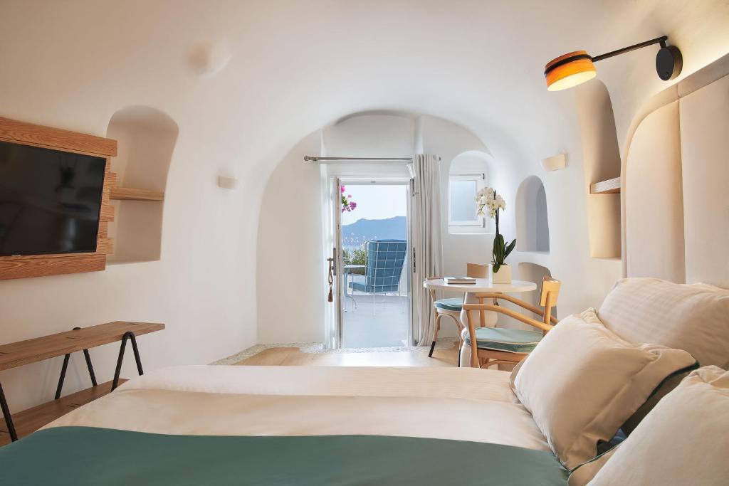 a hotel room with a bed and a table and a television at Katikies Kirini Santorini - The Leading Hotels Of The World in Oia