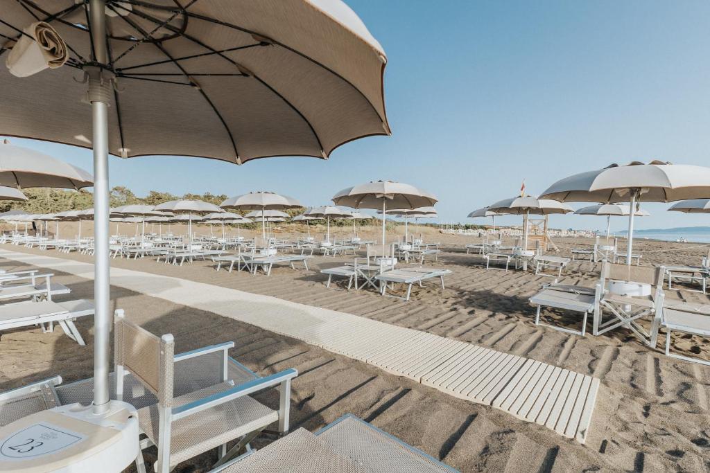 una spiaggia con tavoli, sedie e ombrelloni di Tuscany Hotel Alle Dune a Marina di Castagneto Carducci