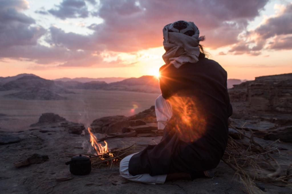 una mujer sentada junto a una fogata con la puesta de sol en Bedouins life camp, en Áqaba