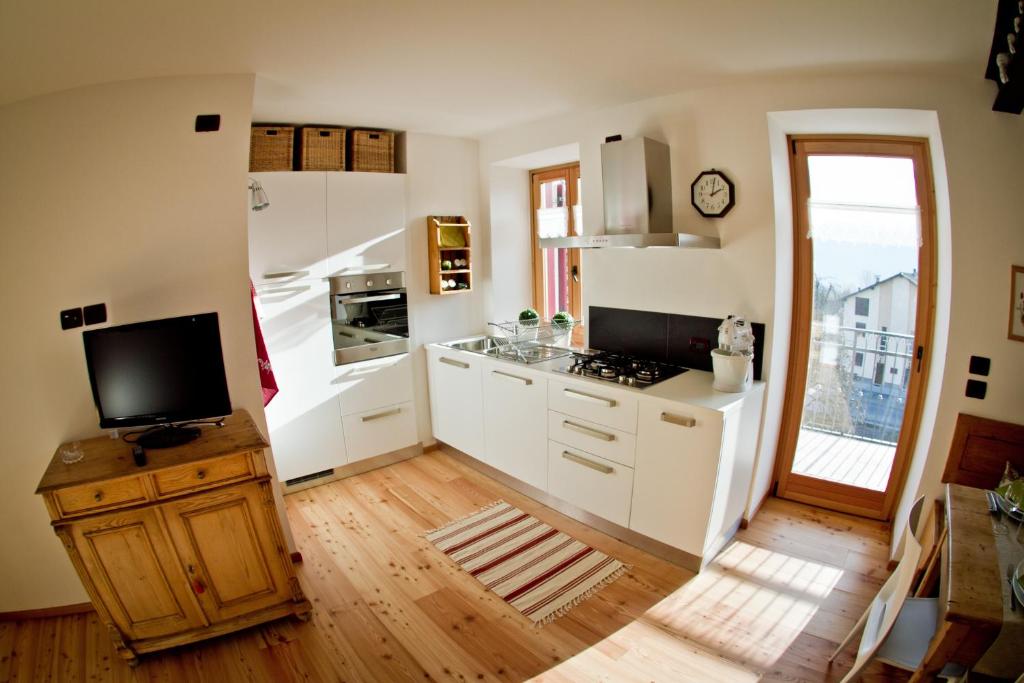 a kitchen with white cabinets and a tv on a wooden floor at Tesino Appartamenti 2 in Castello Tesino