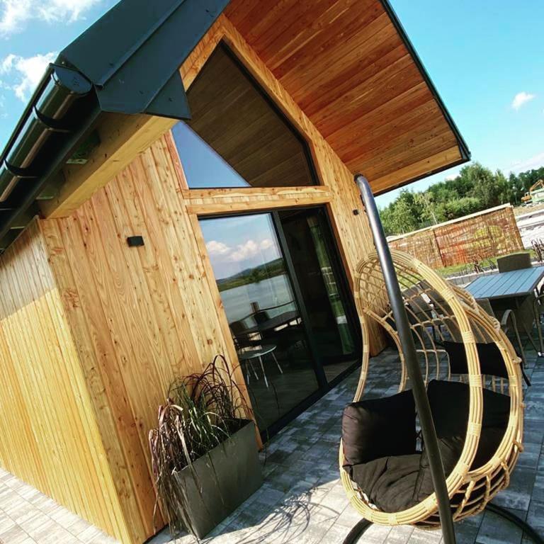 Exterior wooden cabin patio with suspended rattan egg chair and lake view reflection.