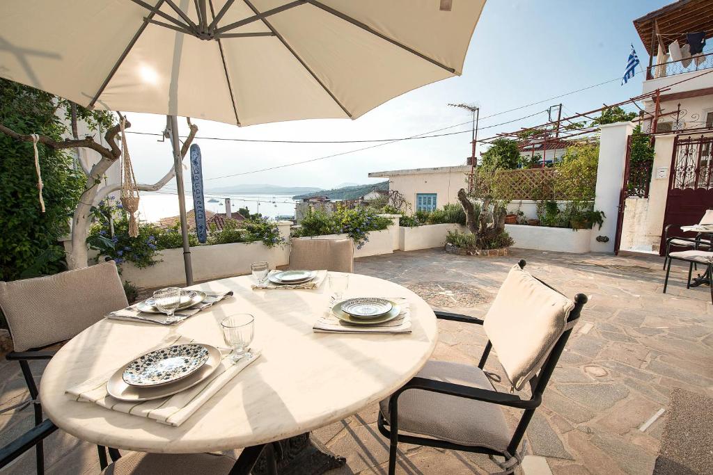 una mesa blanca con sillas y una sombrilla en el patio en Aquarella-Fairytale Apartment with Sunset View, en Poros