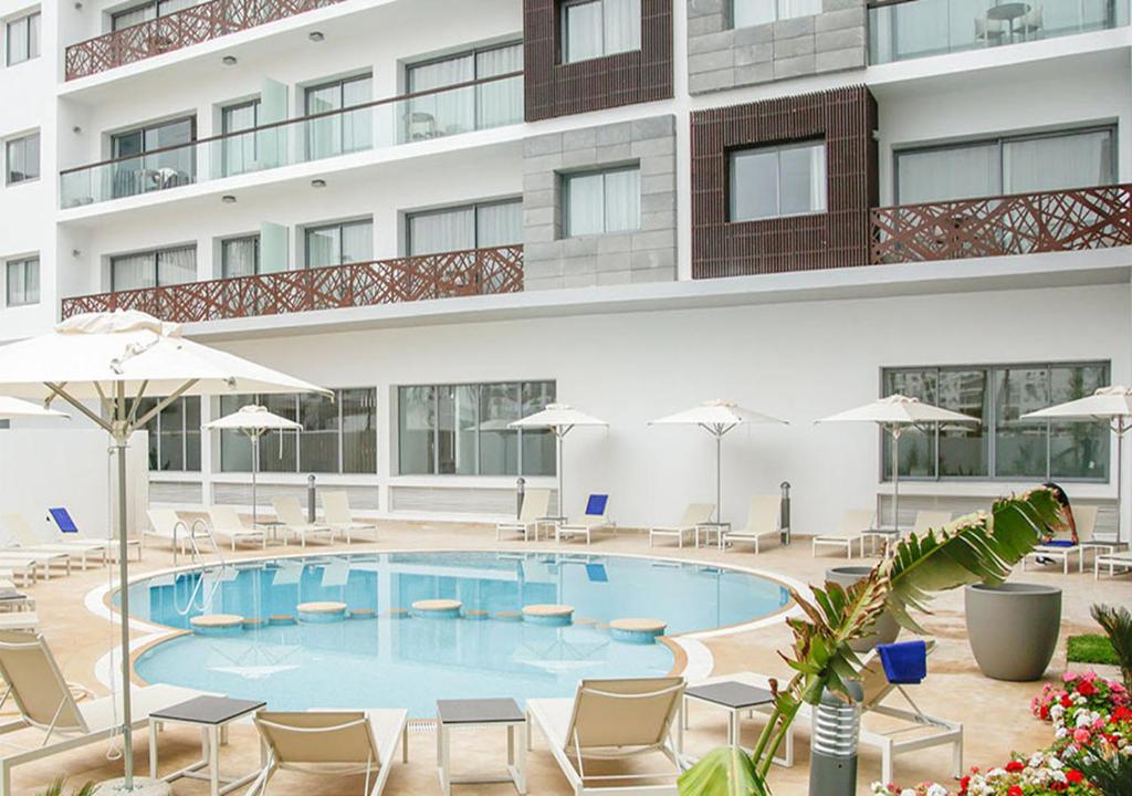 a swimming pool in front of a building with chairs and umbrellas at Zephyr Agadir in Agadir