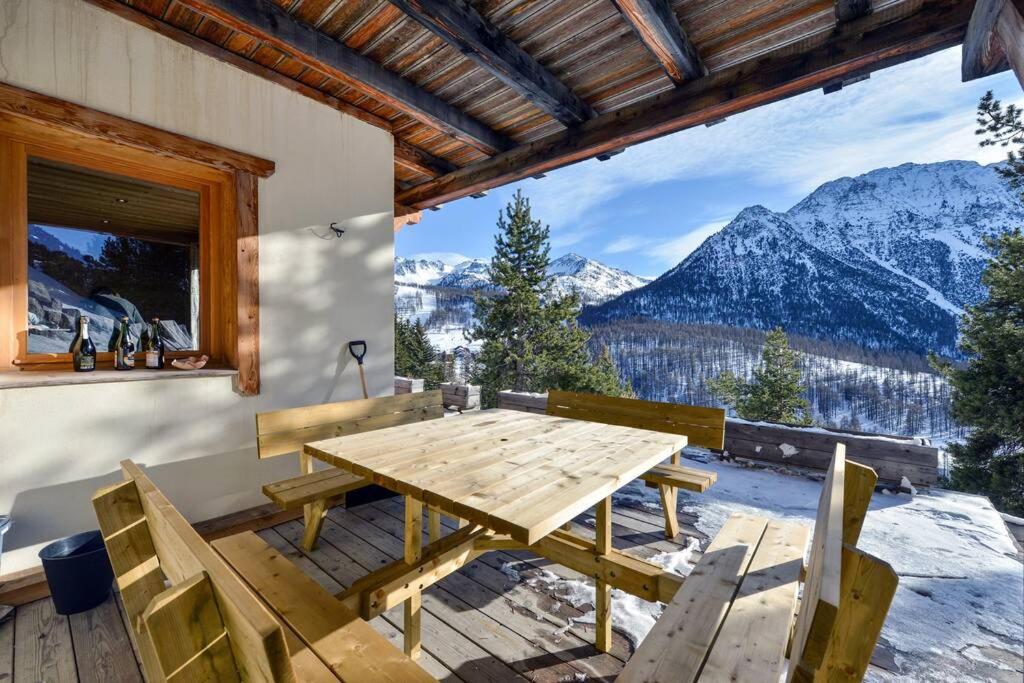 a wooden table and chairs on a patio with mountains at Cosy Mountain _ free park in Montgenèvre