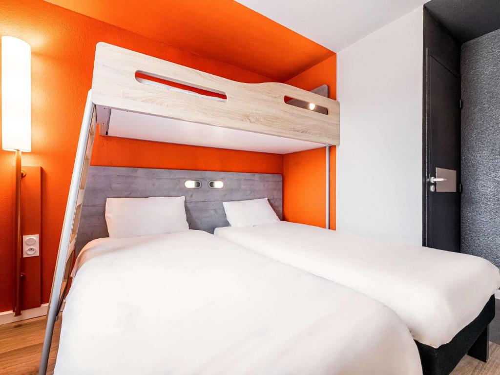 2 łóżka w pokoju z pomarańczową ścianą w obiekcie Ibis Budget Perpignan Sud w Perpignanie