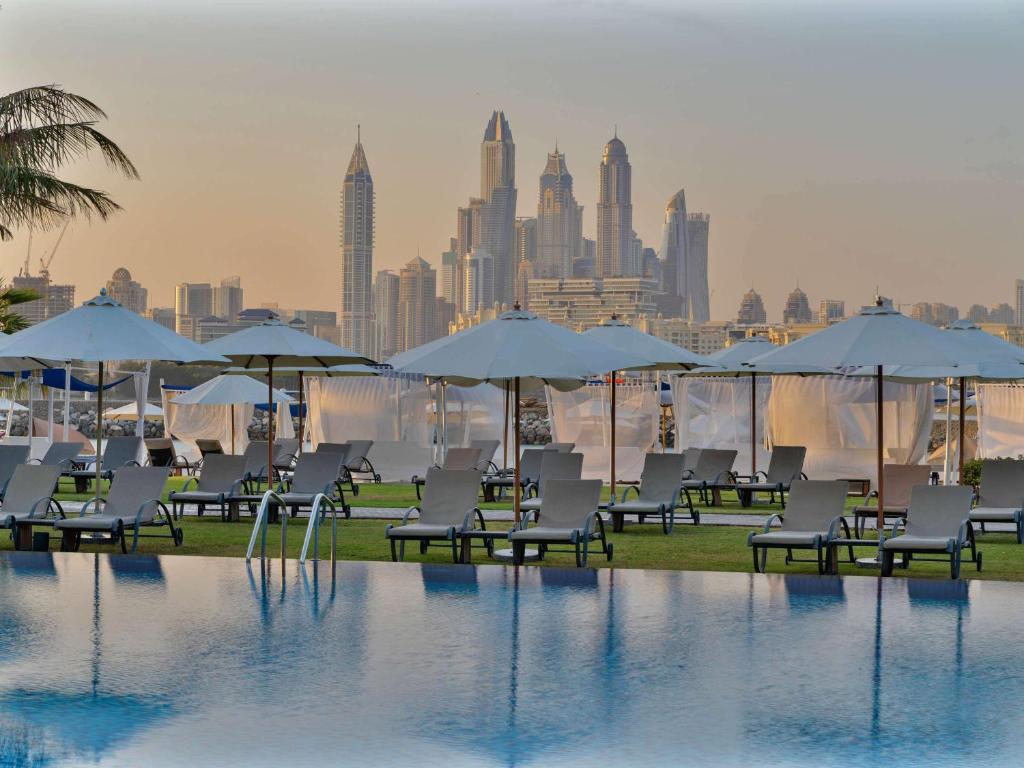 a pool with chairs and umbrellas and a city skyline at Rixos The Palm Luxury Suite Collection - Ultra All Inclusive in Dubai