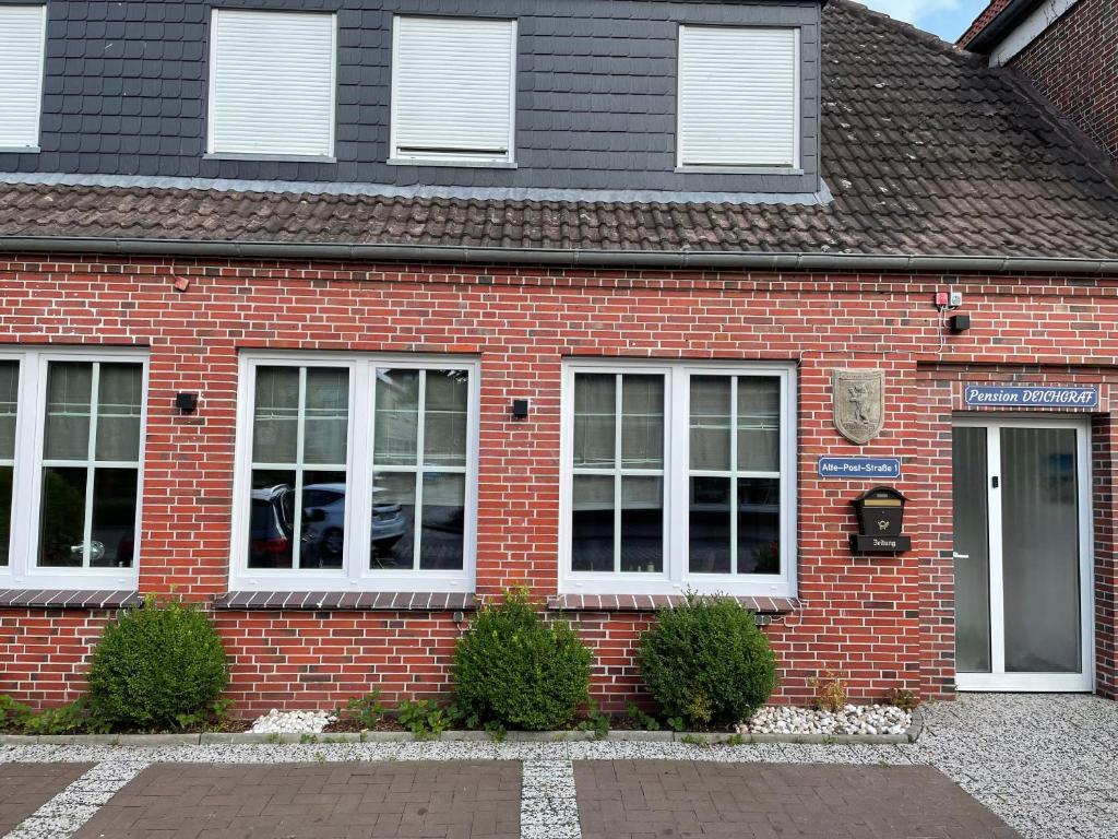 una casa de ladrillo rojo con ventanas blancas y una puerta en Pension Deichgraf, en Dornum