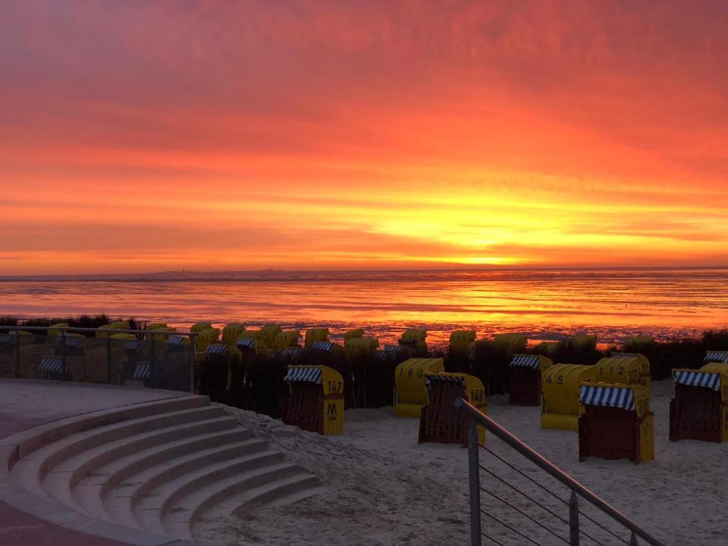 einen Sonnenuntergang am Strand mit Stühlen und dem Meer in der Unterkunft Deichblick in Cuxhaven