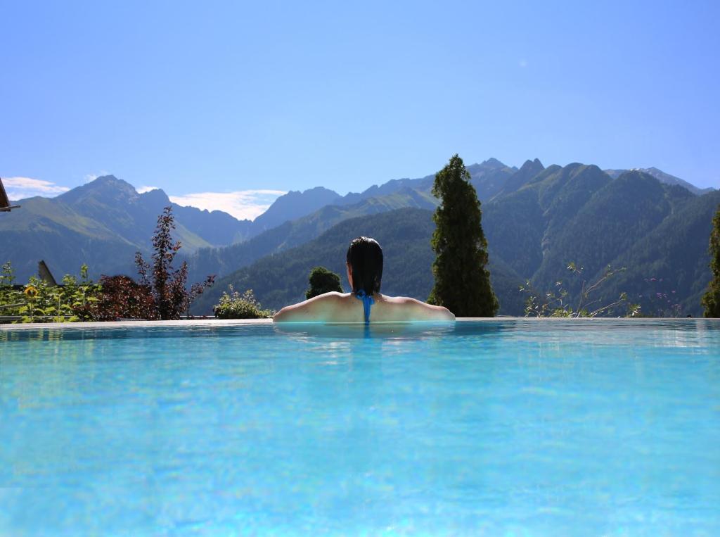 a woman sitting in a swimming pool with a view of mountains at Hotel Pension Geiger in Serfaus
