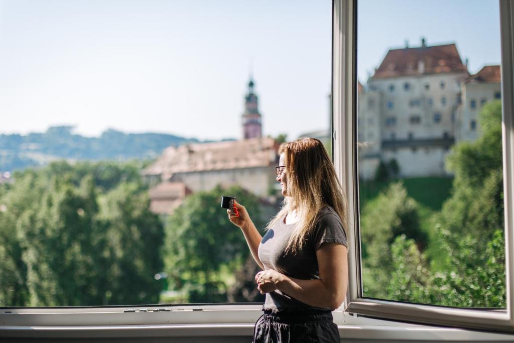 una mujer parada frente a una ventana mirando su celular en CK-Apartment, en Český Krumlov