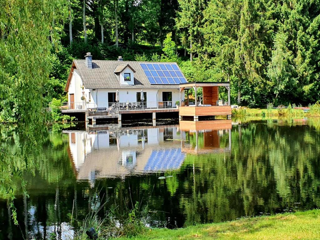 a house with a solar panel on the water at Les étangs du Thioux GUEST HOUSE in Malmedy