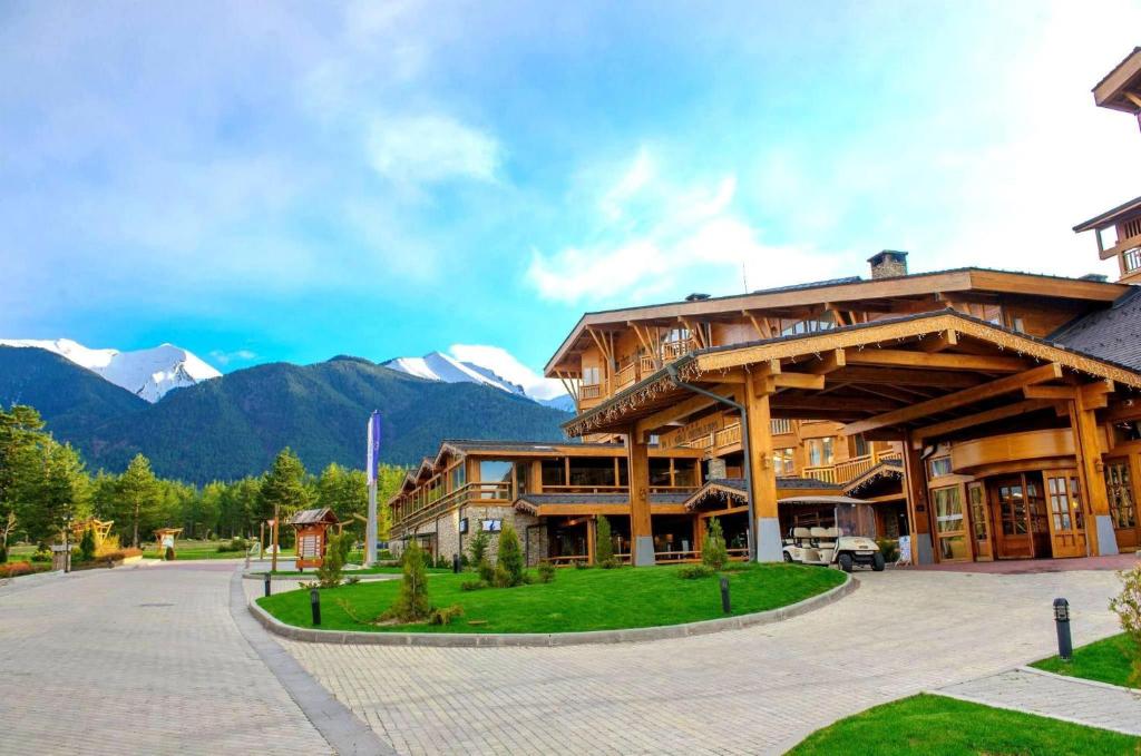 a large wooden building with mountains in the background at Pirin Golf Hotel Private Studios - Sani, Bansko in Razlog