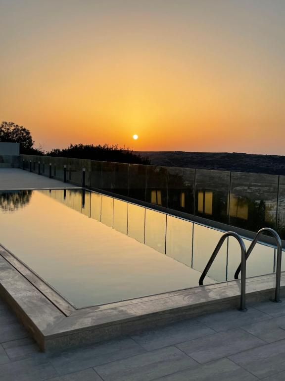 a swimming pool with the sunset in the background at Hotel VIU57 in Mellieħa