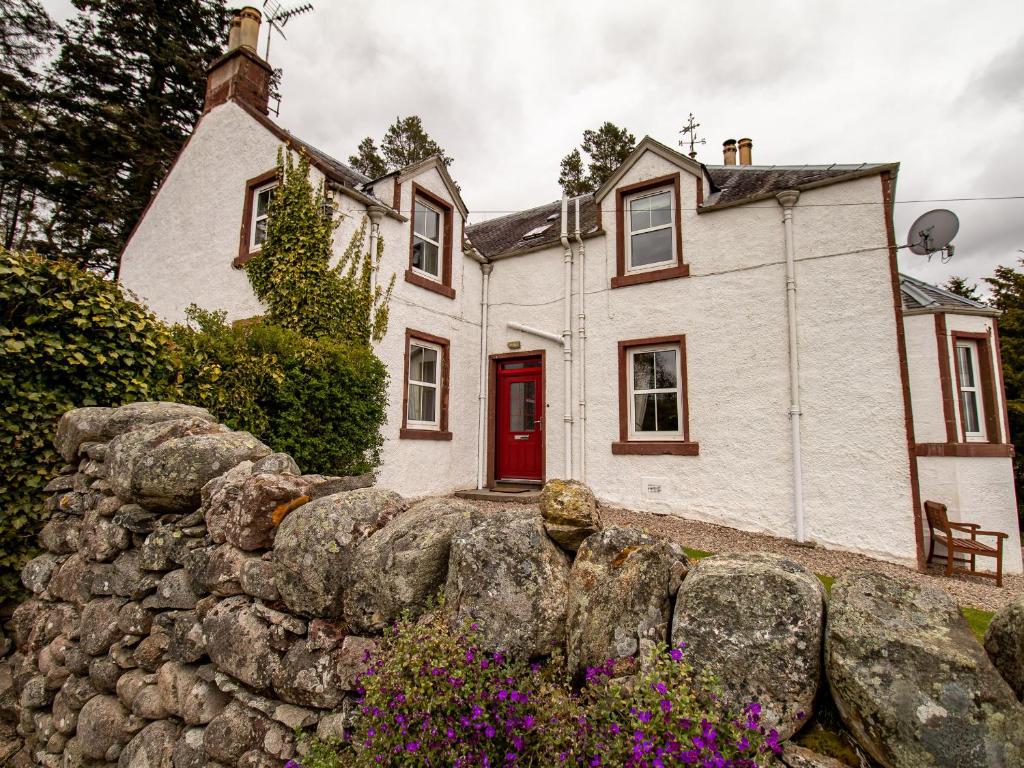 a white house with a red door and a stone wall at Rottal Farmhouse in Millton of Clova