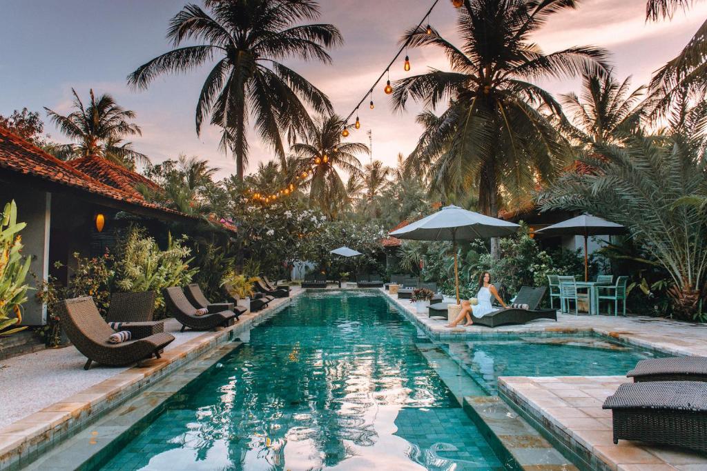 una piscina en un complejo con personas sentadas en tumbonas en Belukar Villas, en Gili Trawangan