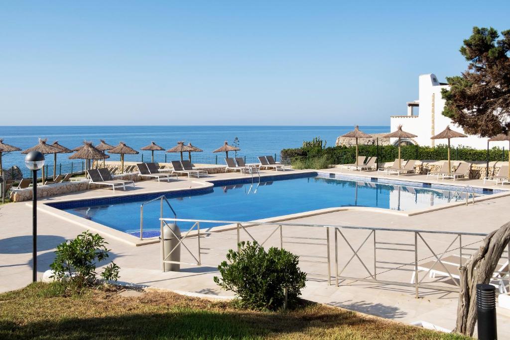 a pool with chairs and umbrellas next to the ocean at Alua Suites Las Rocas in Cala d´Or