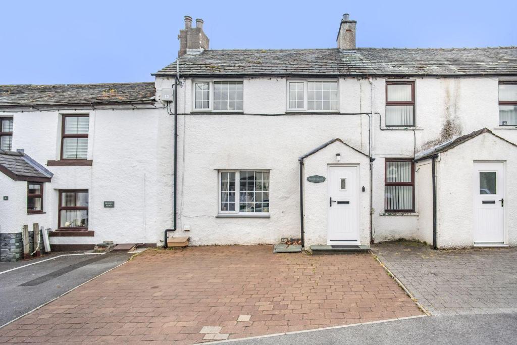 a white house with a white door on a street at Millside Cottage in Braithwaite