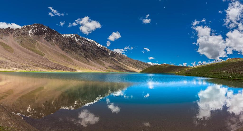 a mountain lake with its reflection in the water at The Nomad's Cottage-Losar , nearest hotel stay to visit Chandra Tal - Lake , in Spiti Valley in Losar