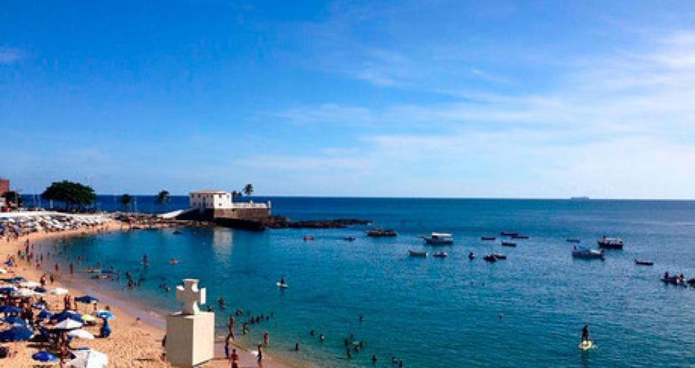 a beach with people in the water and boats at Farol da Barra express - suítes in Salvador