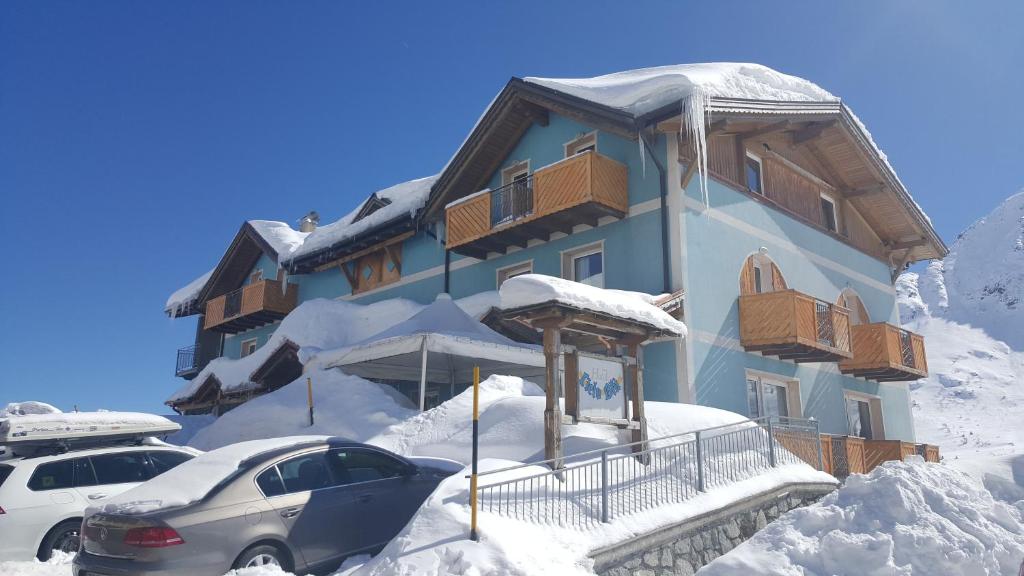 un bâtiment recouvert de neige avec des voitures garées devant dans l'établissement Hotel Cielo Blu, à Passo del Tonale