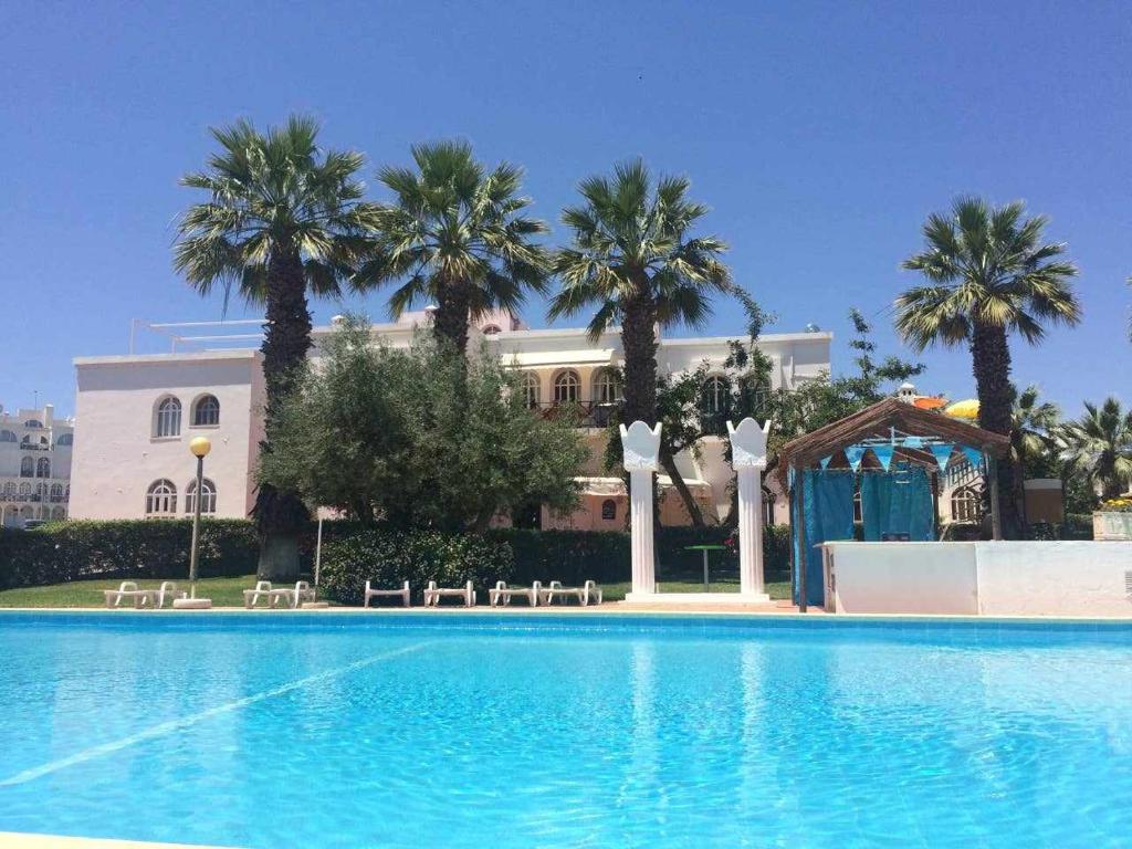 a swimming pool with palm trees in front of a building at Tavira Small cozy flat by the pool and by the sea in Tavira