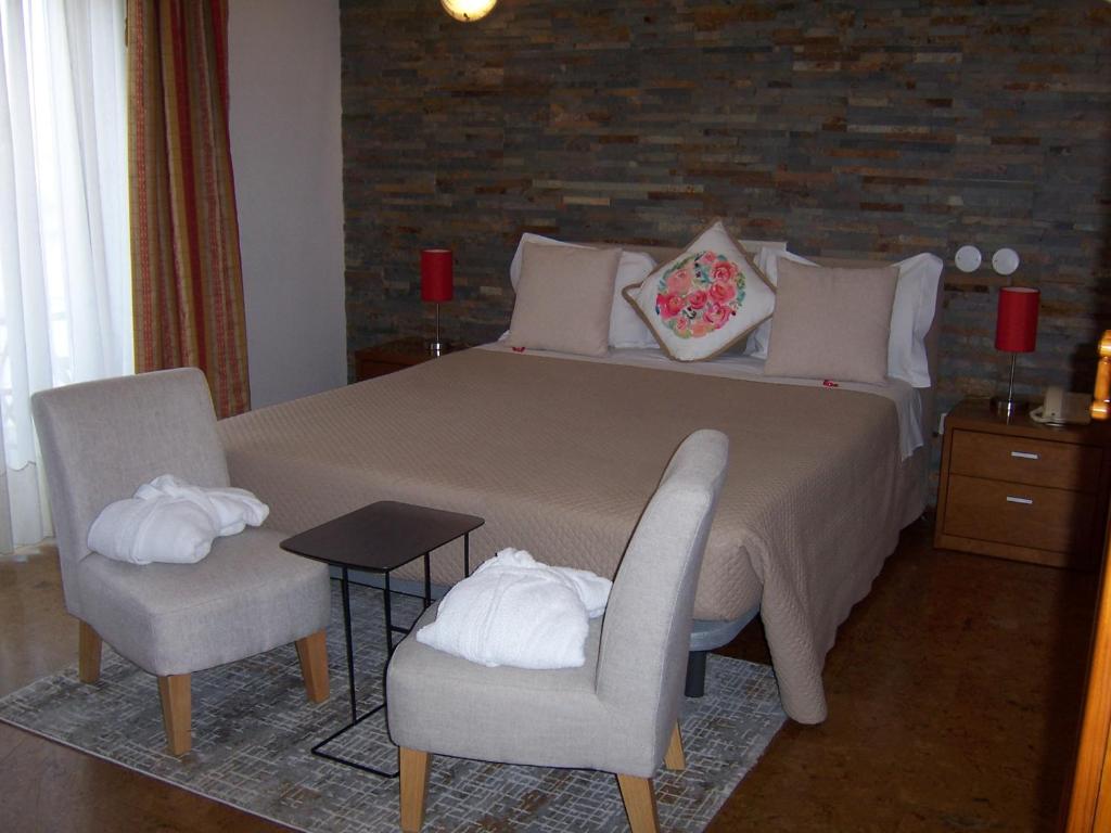 a bedroom with a large bed with two chairs at Hotel Santa Apolonia in Bragança
