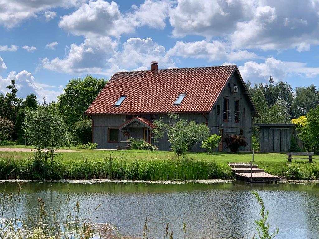 a house with a red roof next to a pond at Pie Ezerrozēm in Kavari