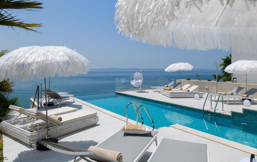 - une piscine avec chaises longues et parasols et l'océan dans l'établissement Gallery Luxury Suites & Rooms-Only Adults, à Split