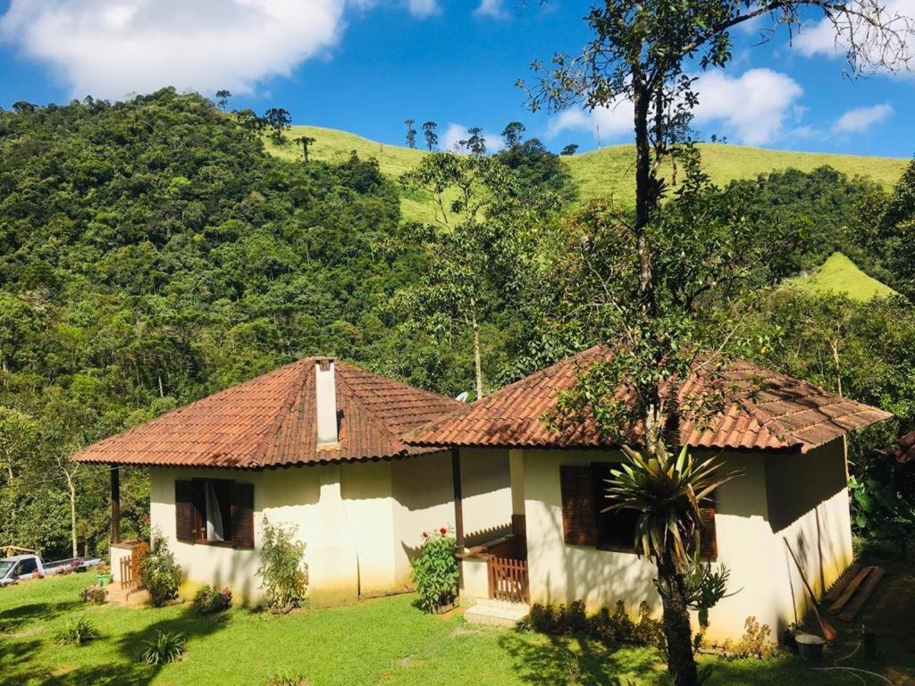 a house in a field with a mountain in the background at Pousada Algama in Visconde De Maua