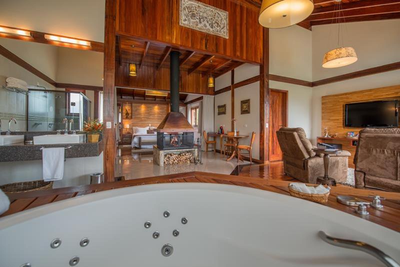 a large bathroom with a tub and a living room at Mirante da Colyna Hotel & SPA in Monte Verde