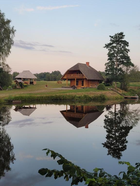 a house sitting next to a lake with its reflection at Brīvdienu māja ar pirti "Strautkalni" in Ieriķi