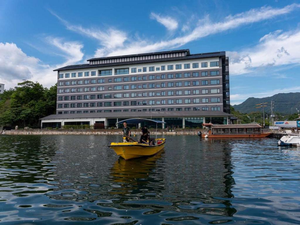 a yellow boat in the water in front of a building at Grandvrio Hotel Miyajima Wakura - ROUTE INN HOTELS - in Hatsukaichi