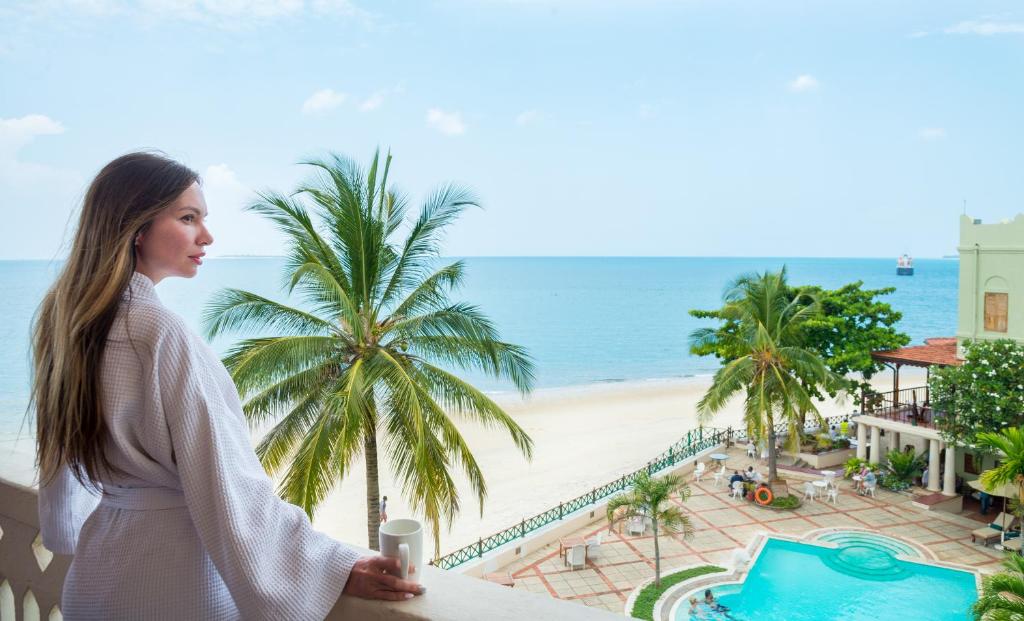 Eine Frau steht auf einem Balkon mit Blick auf den Strand in der Unterkunft Zanzibar Serena Hotel in Zanzibar City