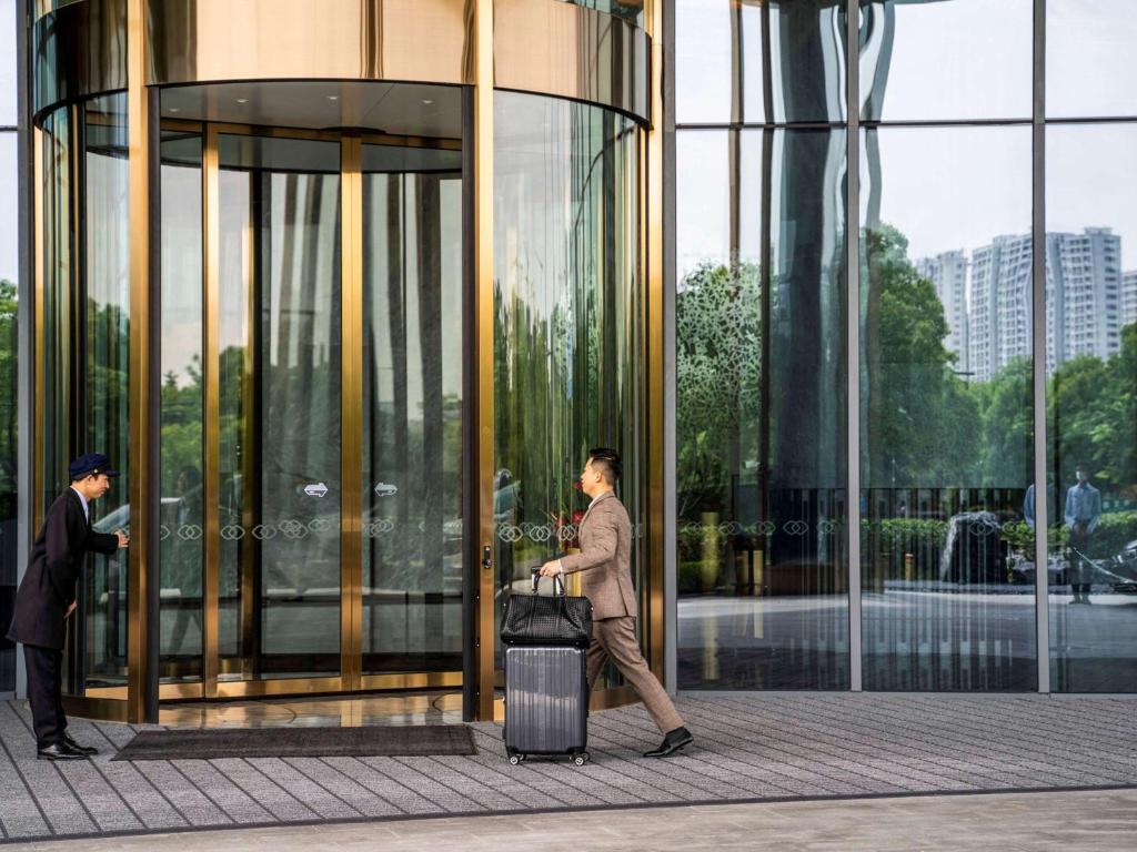 a man walking past a glass building with a suitcase at Sofitel Hangzhou Yingguan in Hangzhou