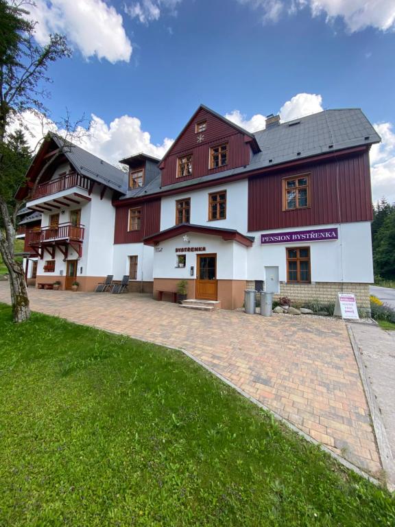 un grand bâtiment rouge et blanc avec une pelouse verte dans l'établissement Pension Bystřenka, à Špindlerův Mlýn