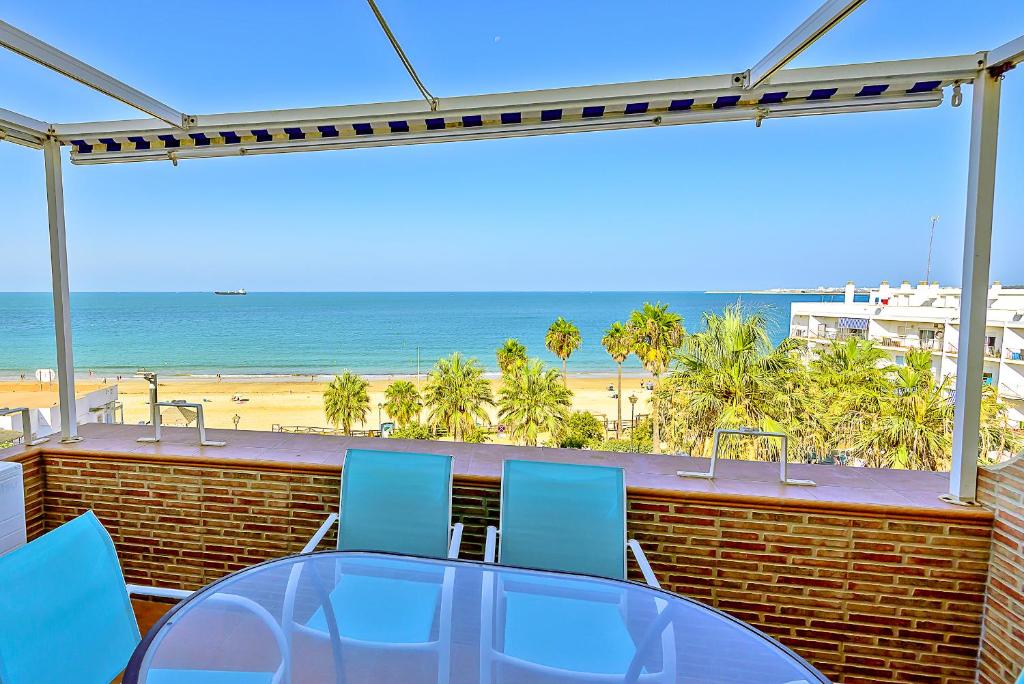 una mesa de cristal y sillas en un balcón con vistas a la playa en Ocean Sunset Beachfront House with Terraces, en El Puerto de Santa María