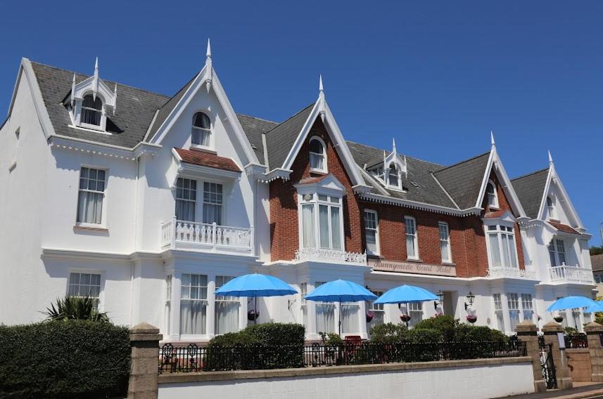 a large white house with blue umbrellas in front of it at Runnymede Court Hotel in Saint Helier Jersey