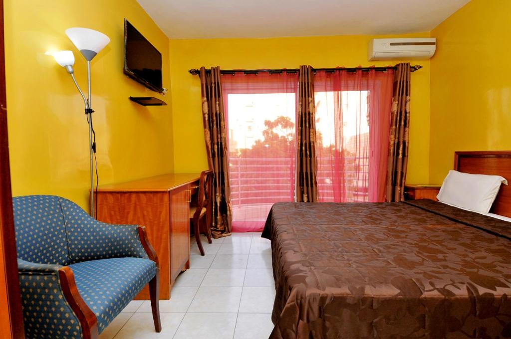 a bedroom with a bed and a chair and a window at Résidence De La Porte Du Millenaire in Dakar